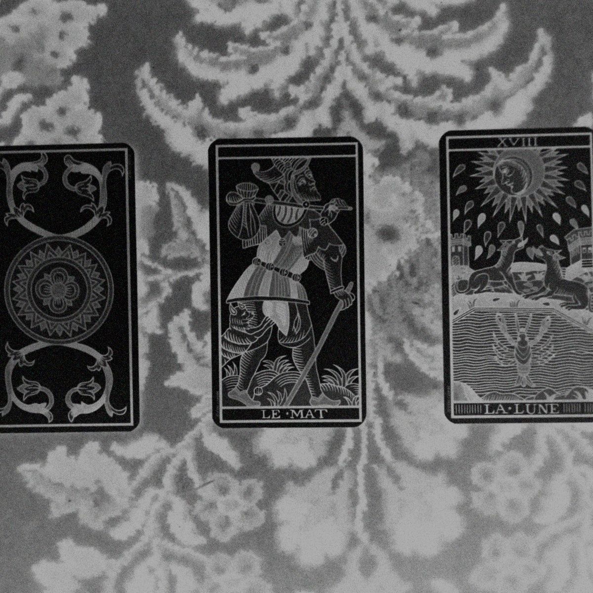 Cover for the track 'hermétique [dronecember]' by REAE. Black and white (inverted) photograph of a tarot reading.